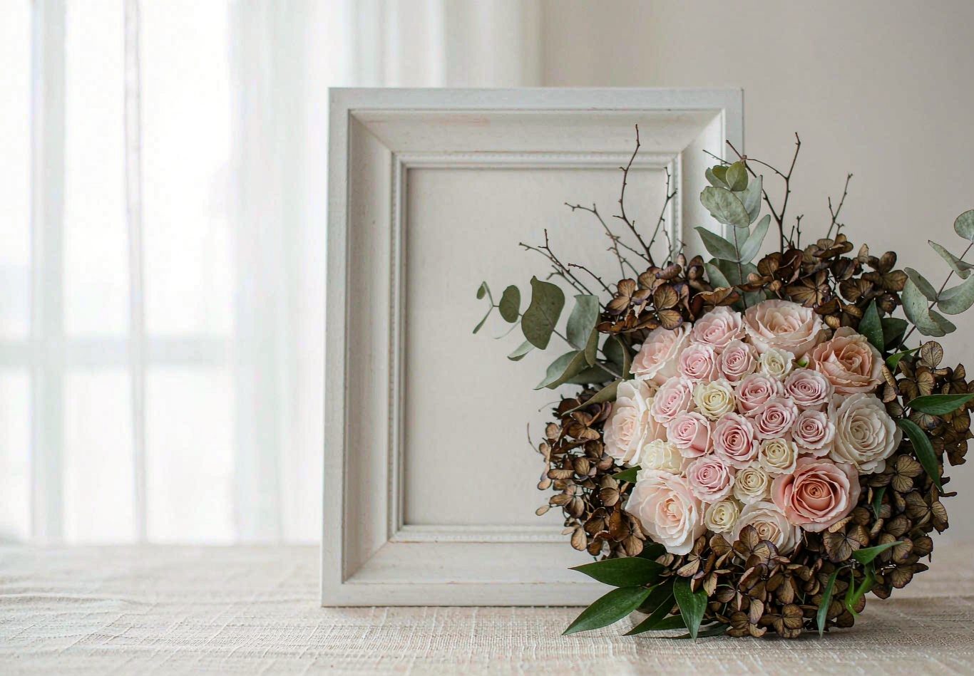 Preserved wedding bouquet beside a white shadow box frame on an ivory linen surface.
